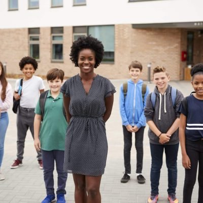 Portrait Of Smiling High School Student Group With Female Teacher Standing Outside School Buildings